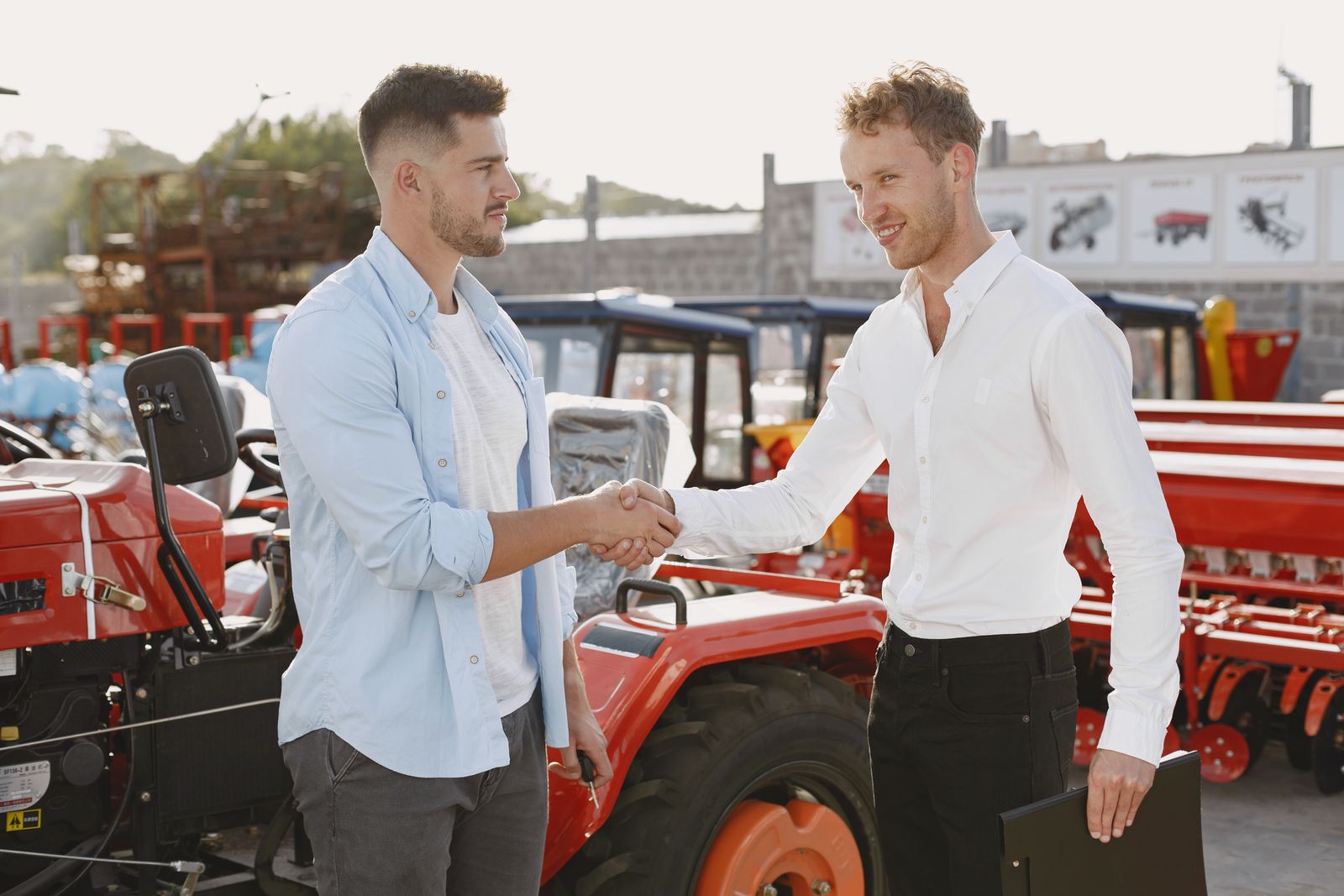 Two people shaking hands in front of a red tractor, at a machinery dealership.